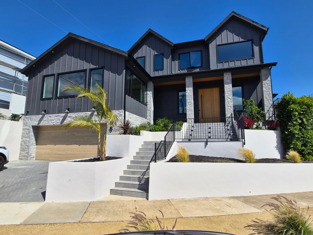 Modern dark gray house with stone accents and wooden garage door.