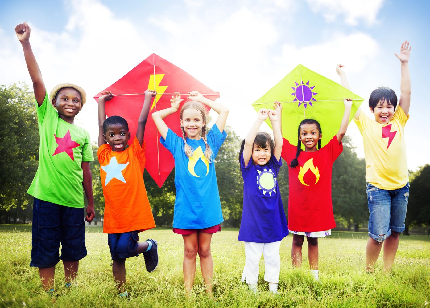 Six children joyfully holding colorful kites in a sunny park.
