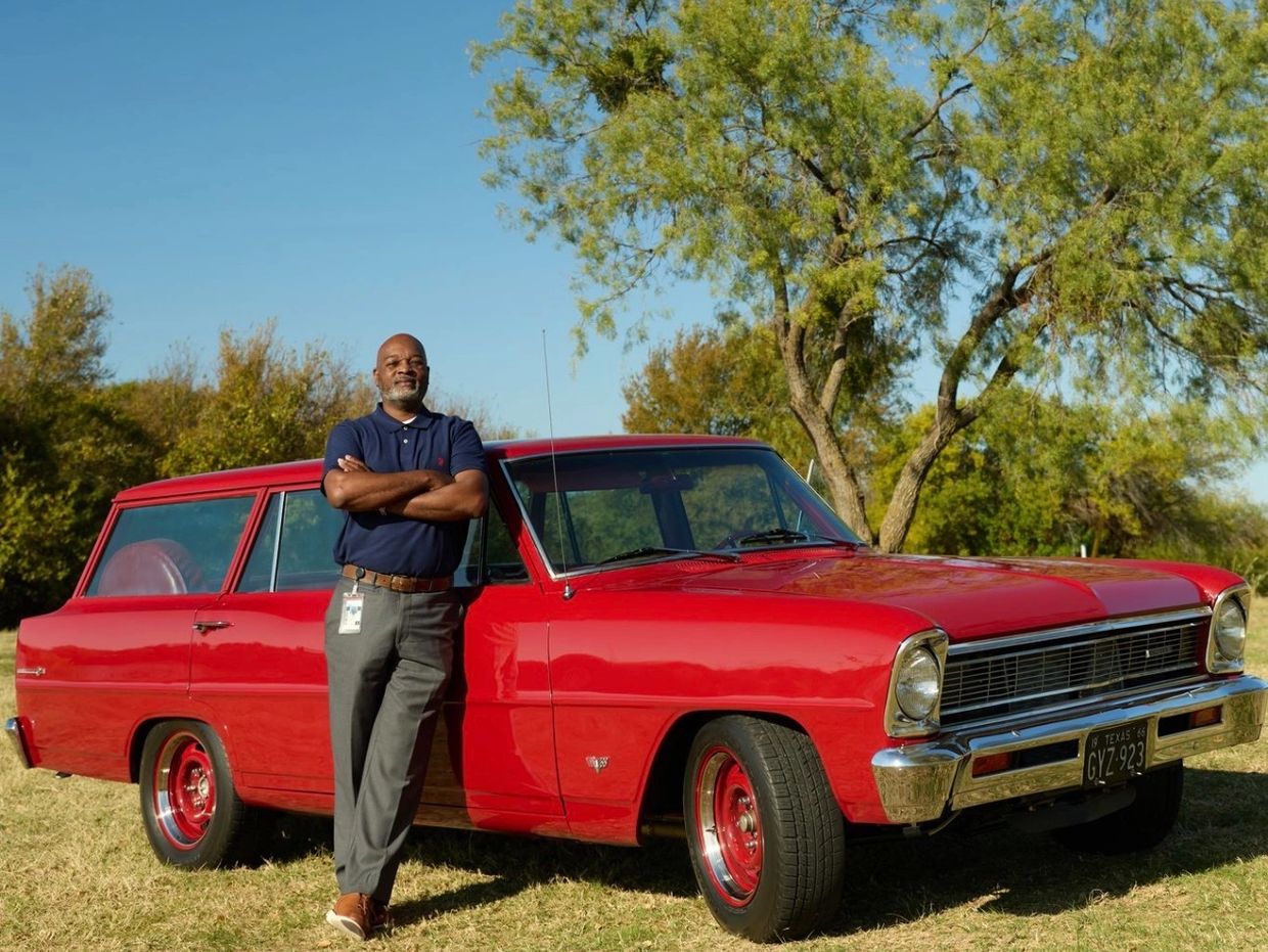 Man posing next to a classic red car.