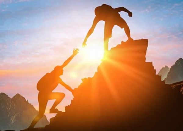 Two hikers helping each other on a mountain at sunset.