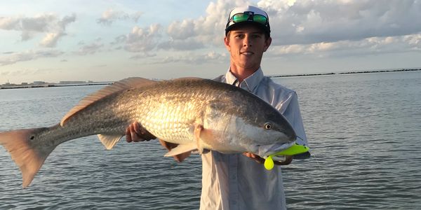 Young man holding a large fish by the water during sunset.