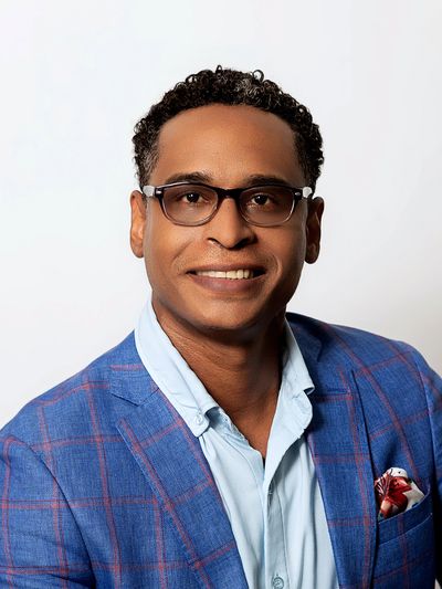 Smiling man in glasses wearing a blue checkered blazer and light blue shirt.
