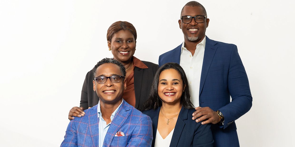 Four professionals smiling confidently in business attire against a white background.
