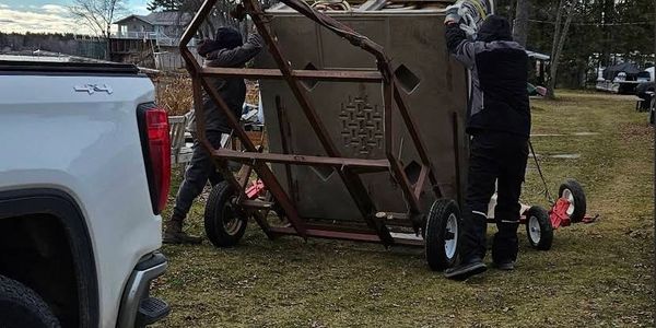 Two people loading a large metal-framed object onto a white truck outdoors.