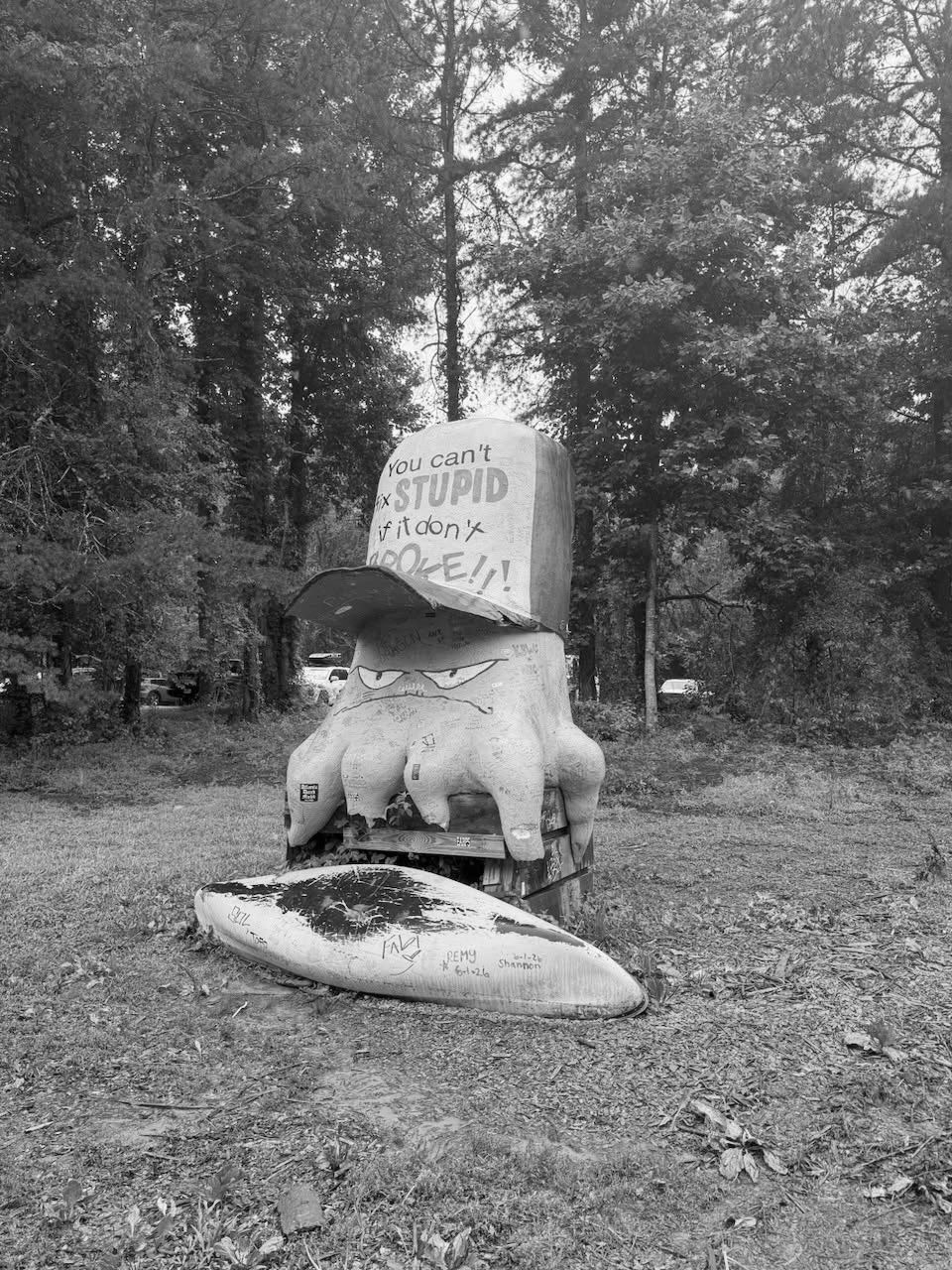 Large quirky sculpture with a humorous hat message in a forest clearing.