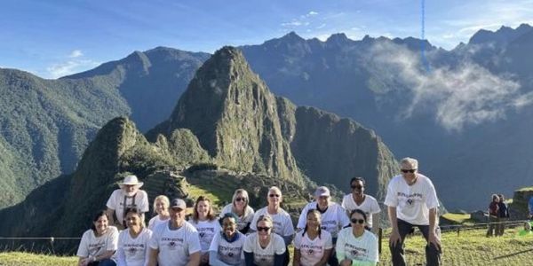 Group of tourists posing in front of Machu Picchu mountain ruins.
