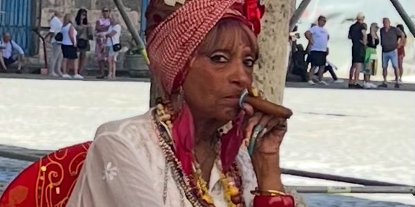 Woman in colorful attire smoking a cigar outdoors.