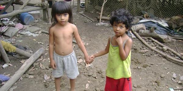 Two young children holding hands in a rustic outdoor setting.