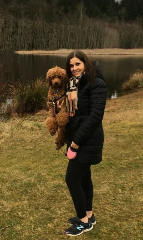 Woman holding a brown poodle by a lake.