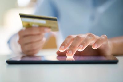 Person using a tablet and holding a credit card for online payment.