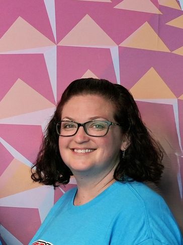 Smiling woman wearing glasses and blue shirt against colorful geometric background.