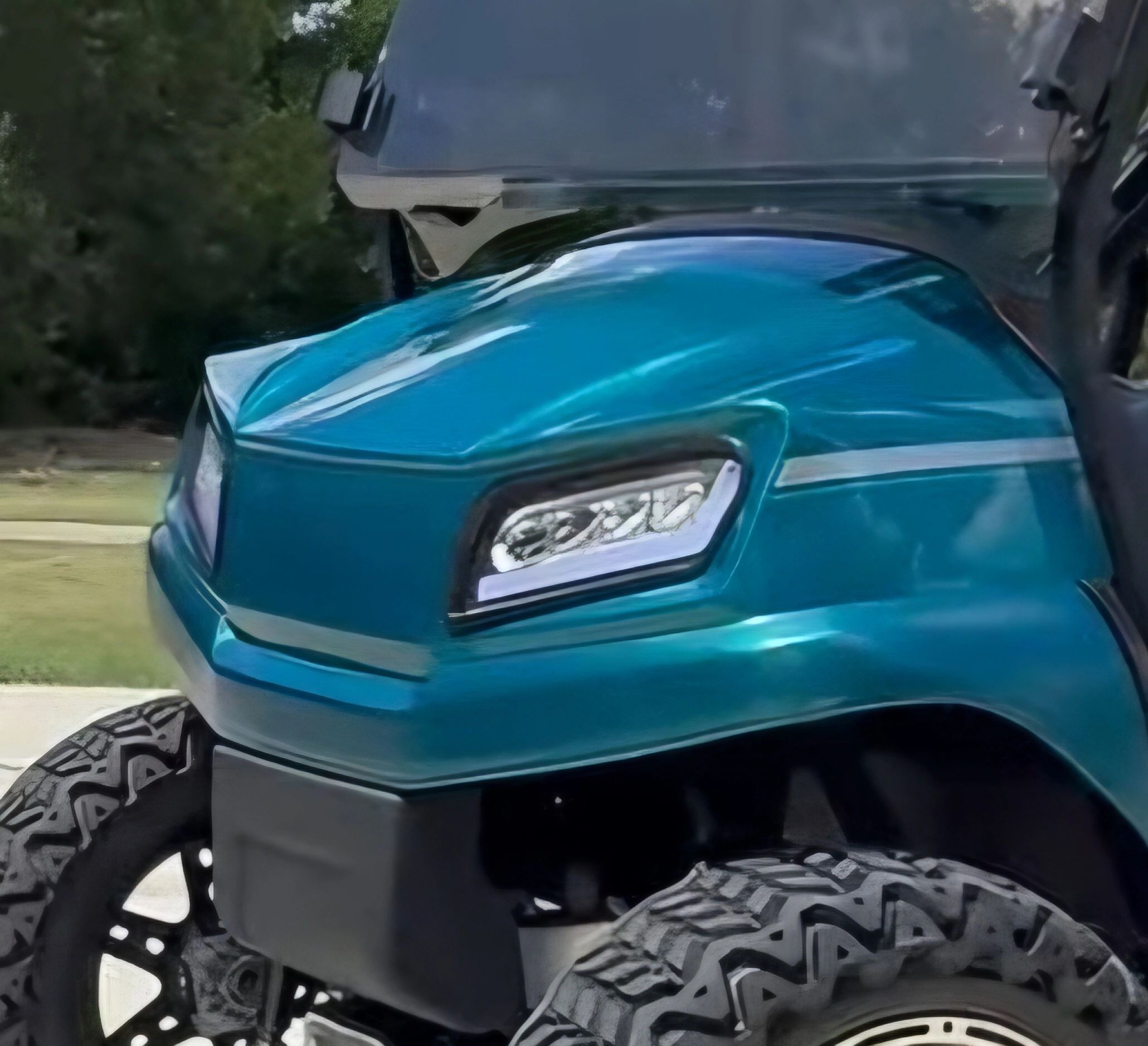 Close-up of a shiny teal off-road vehicle front with rugged tires.