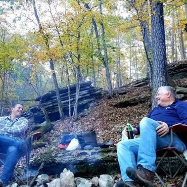people sitting in woods around a campfire
