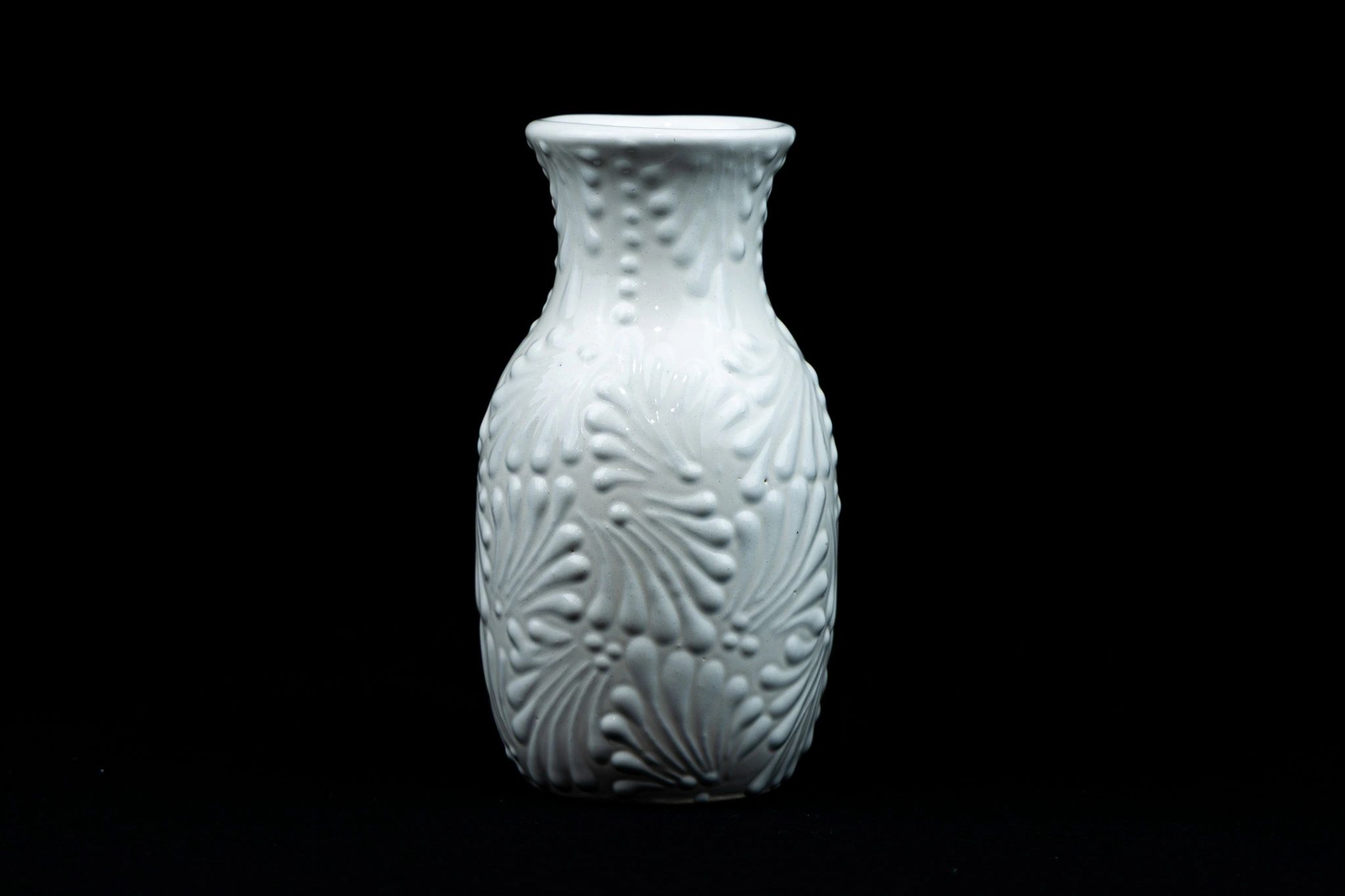 White ceramic vase with intricate floral patterns against a black background.