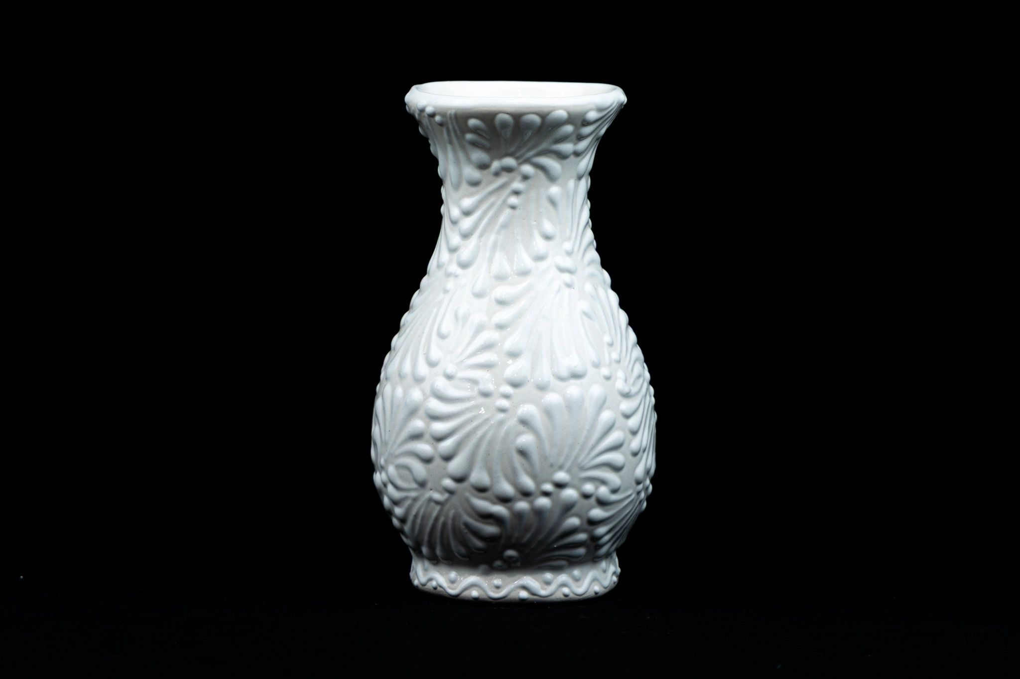 White ceramic vase with intricate raised floral designs against black background.