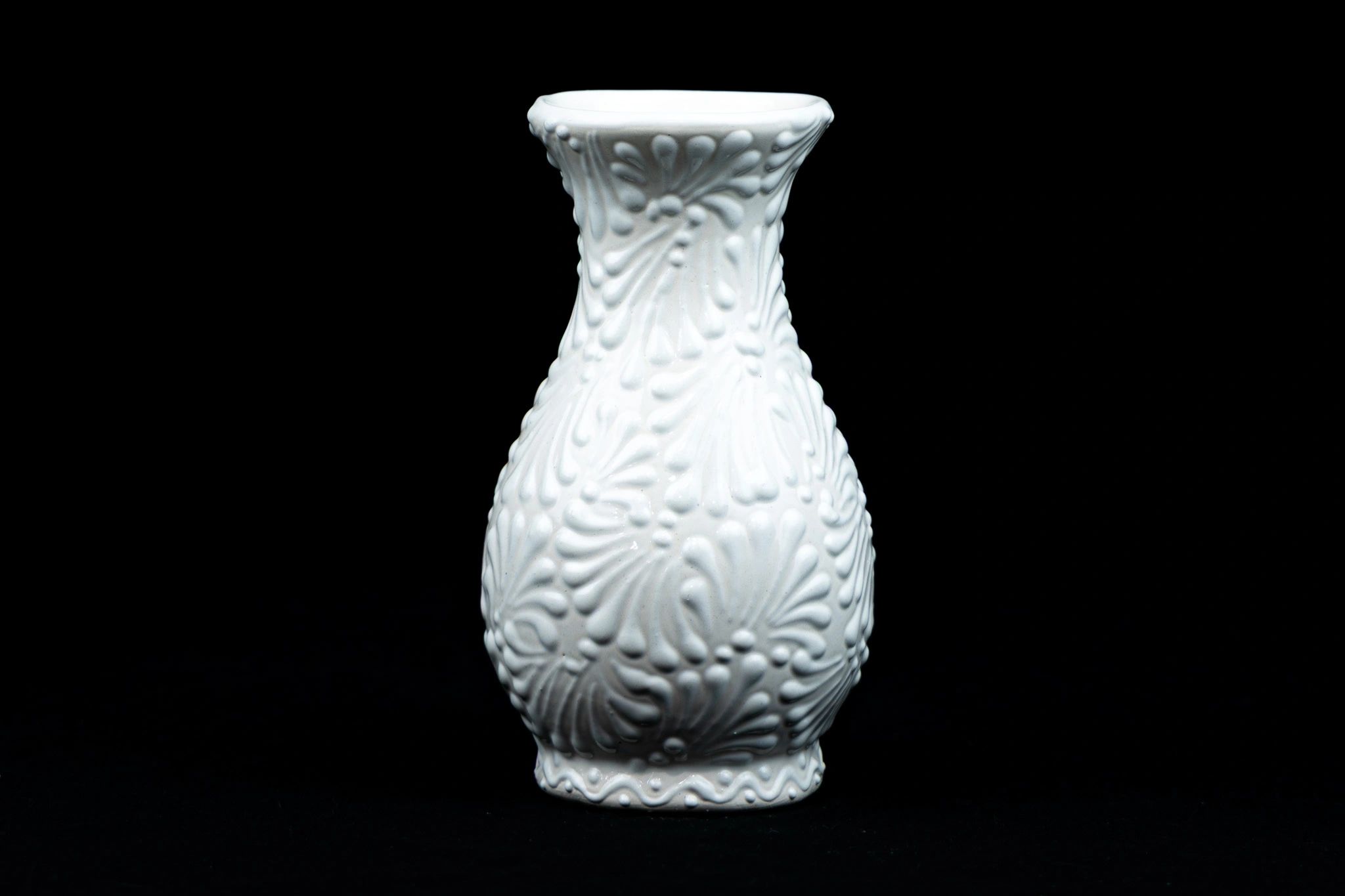 White ceramic vase with embossed floral patterns on a black background.