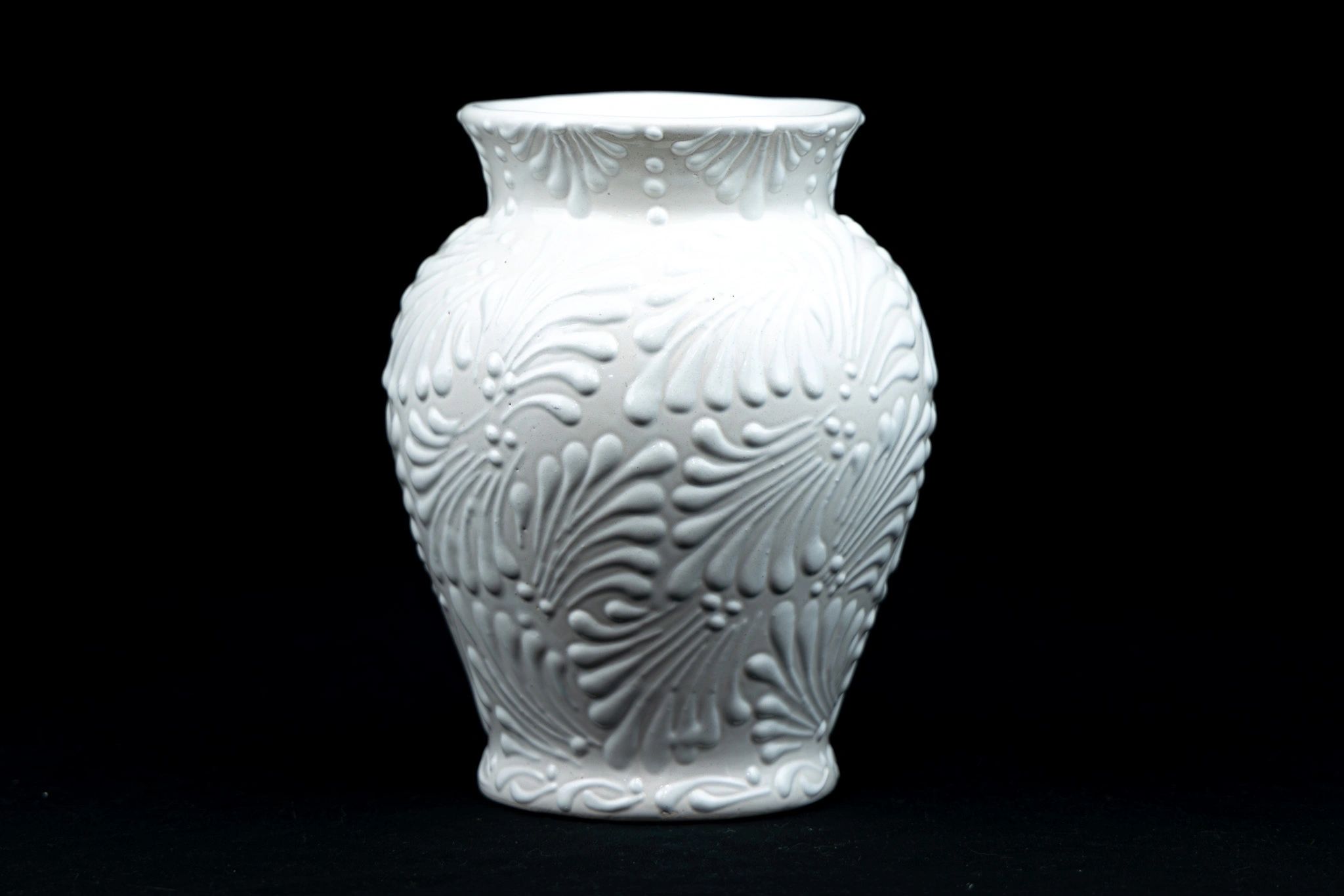 Elegant white ceramic vase with intricate embossed patterns on black background.