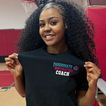 Smiling woman in a gym showing a "Passionate Motivation Coach" t-shirt.