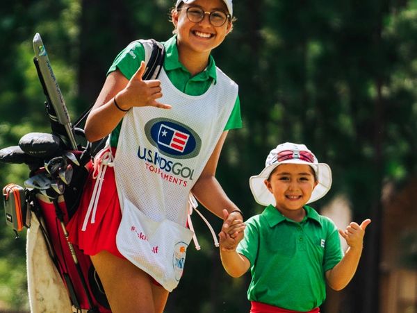 Smiling young golfer and child making shaka signs together on a golf course.
