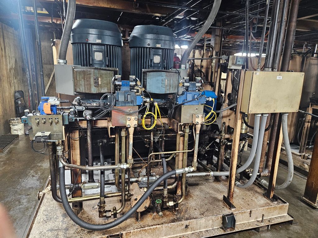 Industrial hydraulic system with motors, valves, and pipes in a workshop.