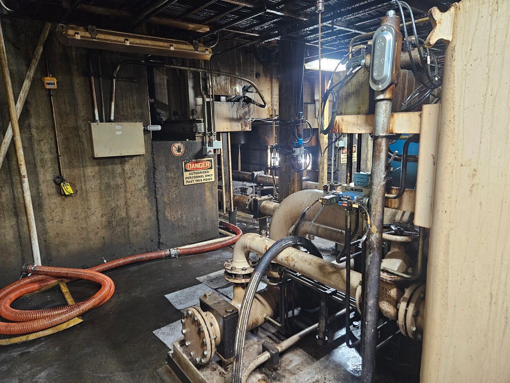 Industrial room with pipes, machinery, and a danger warning sign.