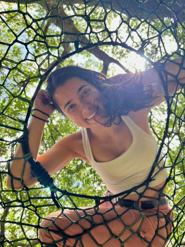 Young woman smiling through a circular net with sunlight and trees behind.