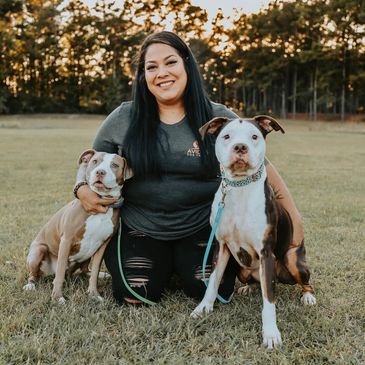 a woman kneeling on the ground in between two pit bull dogs