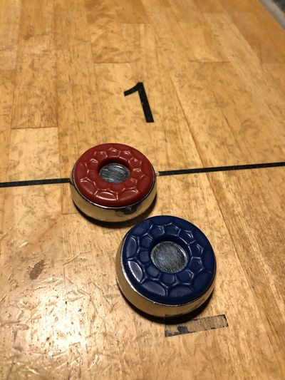 Shuffleboard pucks (red and blue) on a wooden court with the number '1' visible.
