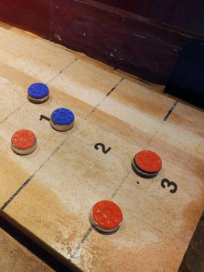 Shuffleboard table with several red and blue pucks scattered across the playing surface.