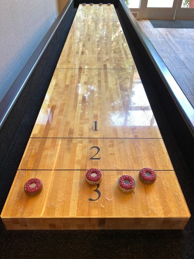 A close-up view of a wooden shuffleboard table with four red pucks and scoring numbers.