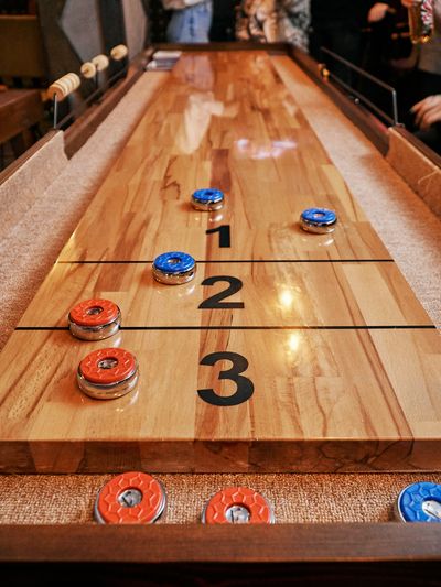 A close-up of a shuffleboard table with red and blue pucks on the numbered scoring zones.