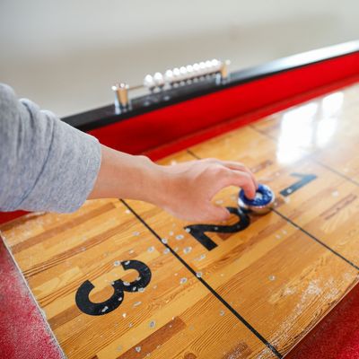 Person playing shuffleboard on a wooden table with red edges and numbered scoring zones.