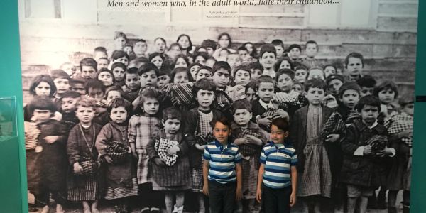 Two boys stand in front of a large black-and-white photo of children.