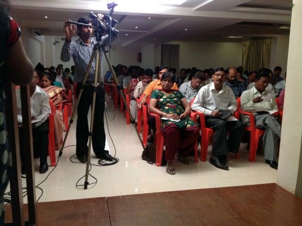 Audience seated in a hall with a cameraman recording the event.