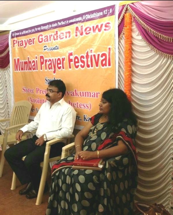 Two people seated at Mumbai Prayer Festival event with a banner behind.