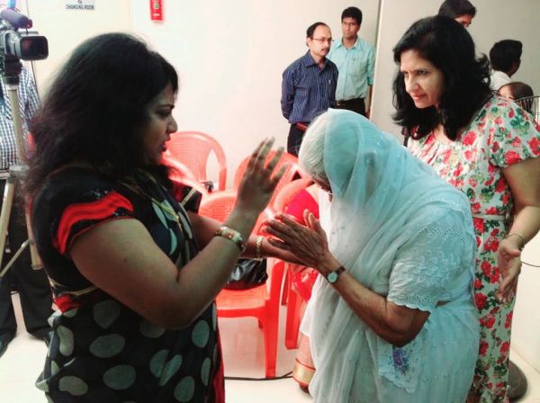 A woman blessing an elderly lady covered in a white sari while others watch.