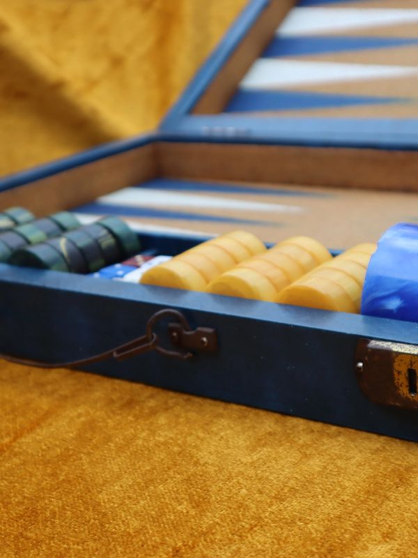 Open backgammon set with colorful game pieces on a golden surface.