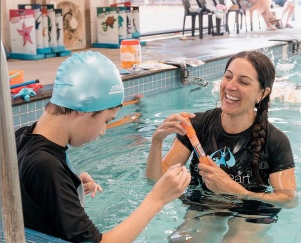 
The image shows two individuals in a swimming pool. On the left, a person wearing a light blue