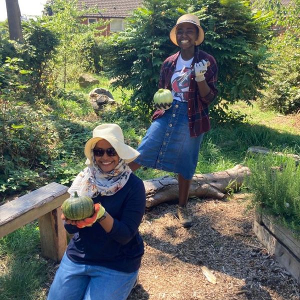 Two people wearing gardening gloves holding vegetables in a natural garden.