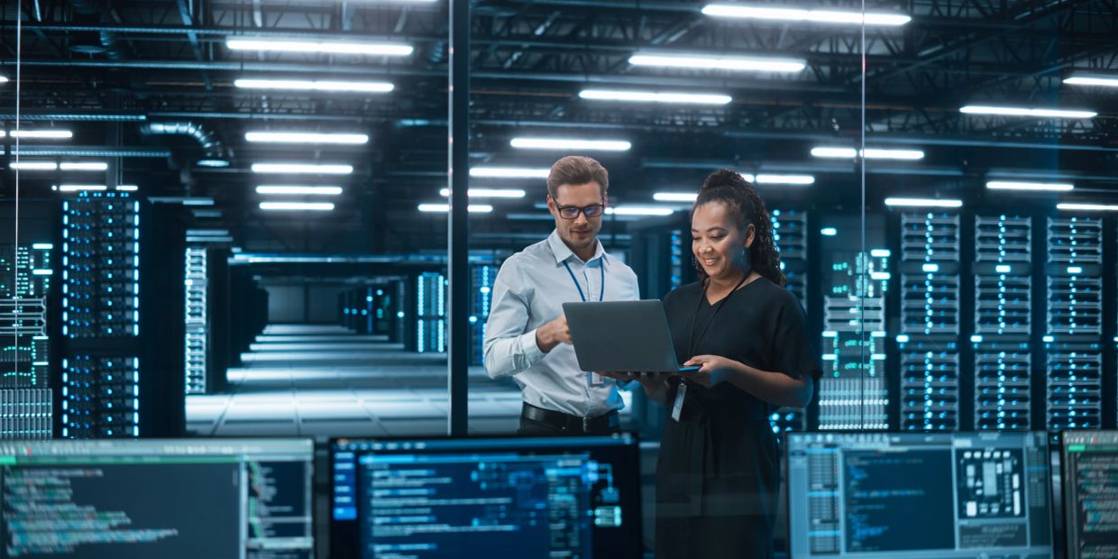Two IT professionals working in a server room with computers and servers.