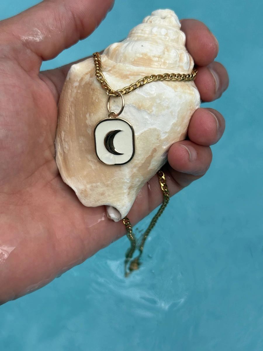 The Golden Hour necklace resting on a seashell beside turquoise water.