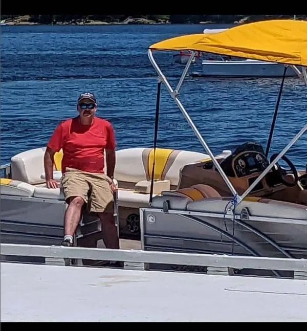 Man in red shirt relaxing on a yellow and white boat by the water.
