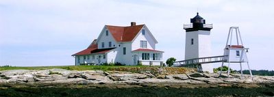 A lighthouse and keeper's house on rocky coastline under a clear sky.