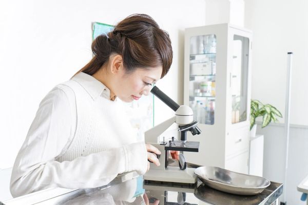 A woman looking through a microscope in a bright lab.