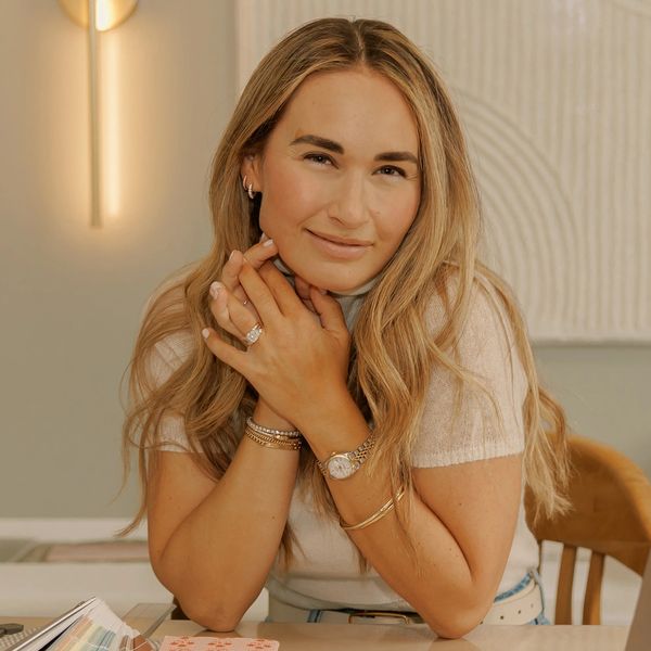 Smiling woman with long blonde hair and elegant jewelry sitting at a table.