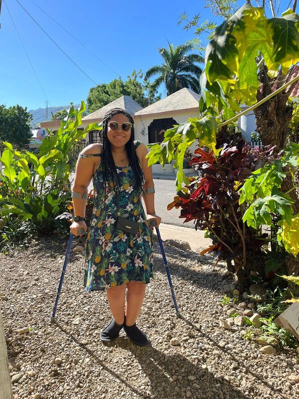 Johileny in crutches wearing hawian flower dress in front of flowers in DR