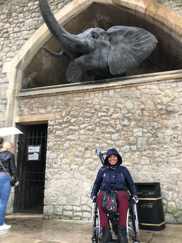 Johileny in the tower of London. In her wheelchair in front of a wall with a statue of elephant head