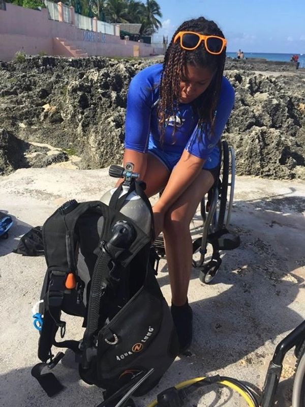 Johileny in wheelchair preparing scuba diving gear.