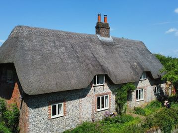 Traditional thatched cottage with chimney under a clear blue sky.