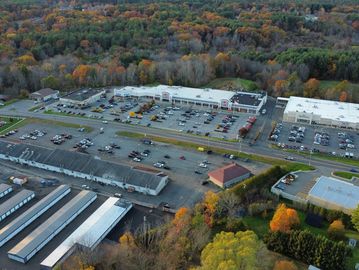 Aerial view of a shopping plaza with parking lots and surrounding autumn trees.